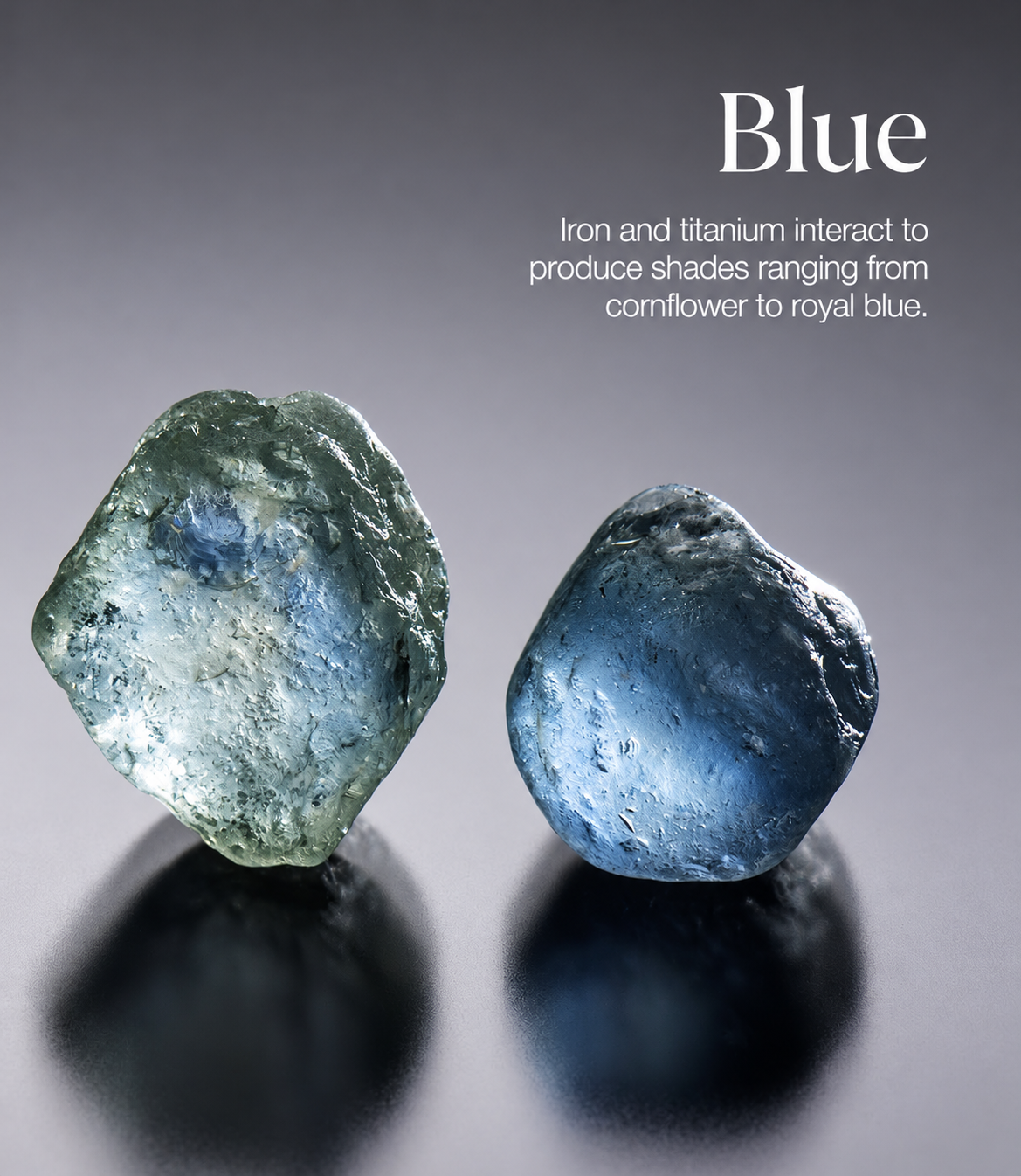 Two rough blue sapphire stones on a grey studio surface